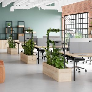 Modern open-plan office space with ergonomic desks, lush green plants in wooden planters, and industrial brick and metal accents, designed for productivity and comfort.