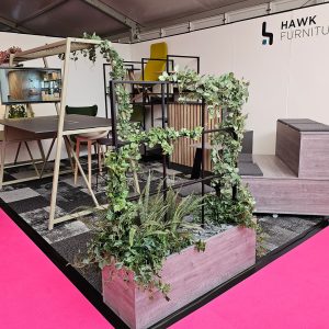 Contemporary furniture display at Chrisbeon exhibition booth, featuring stylish office desks, chairs, and decorative plant arrangements for modern workspace design.